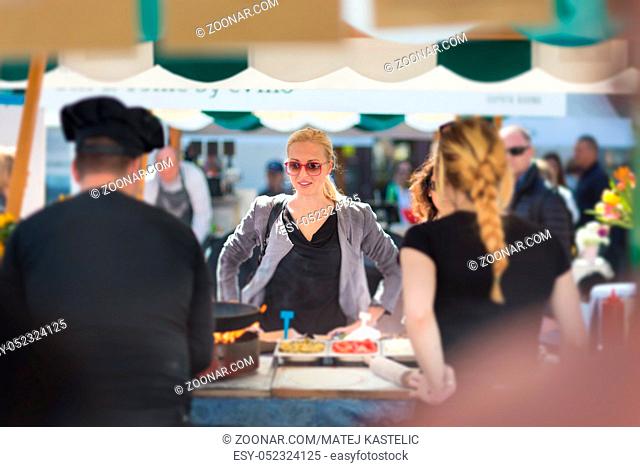 Beautiful blonde caucasian lady buying freshly prepared meal at a local street food festival. Urban international kitchen event in Ljubljana, Slovenia