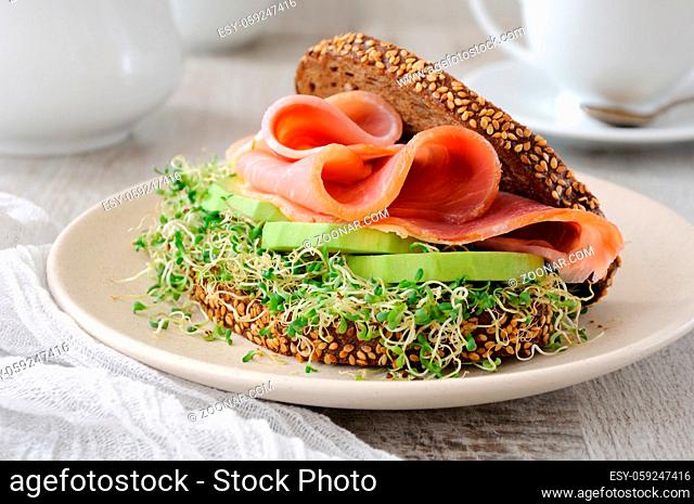 Sandwich of rye bread with cereals, slices of ham and avocado with sprouts of sprouted alfalfa