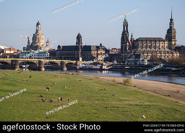 17 April 2020, Saxony, Dresden: People lie at intervals on the Elbe meadows against the historical backdrop of the old town with the Frauenkirche (l-r)