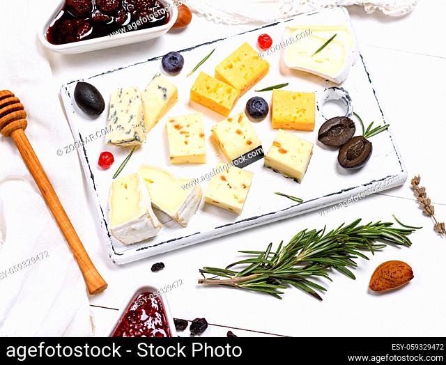 small pieces of brie cheese, roquefort, camembert, cheddar and cheese with walnuts on a white wooden board, top view