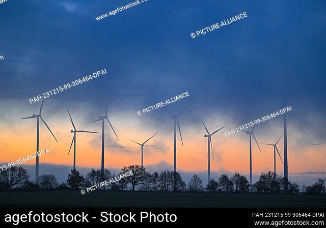 15 December 2023, Brandenburg, Sieversdorf: The morning sky shines over the Odervorland wind farm, while fog and dense clouds drift across the landscape
