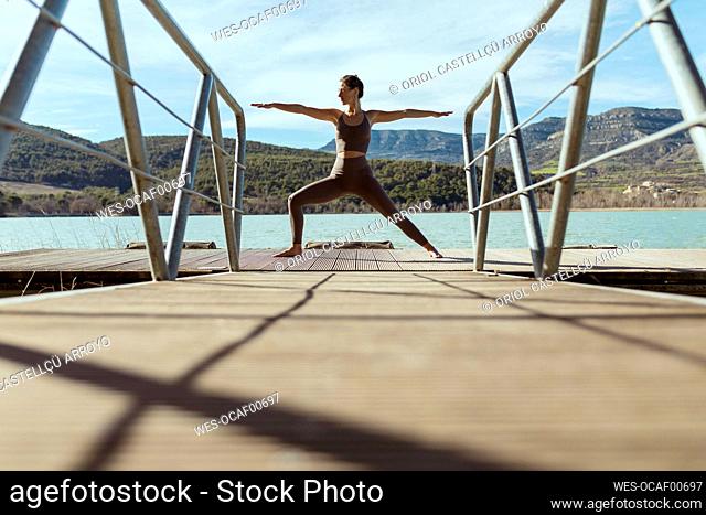 Sportswoman doing Warrior 2 pose on jetty during sunny day