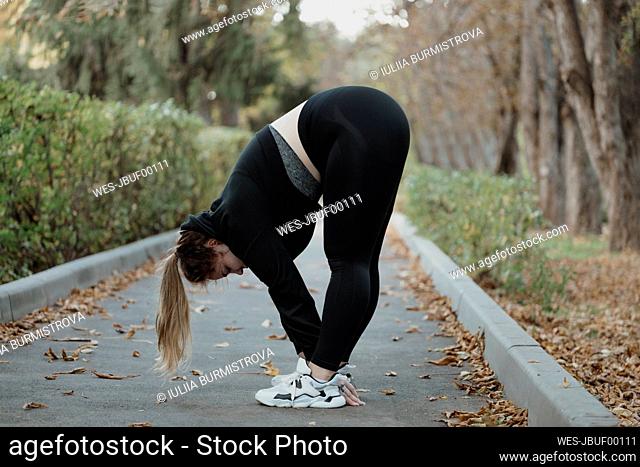Young woman doing stretching exercise on footpath in autumn park