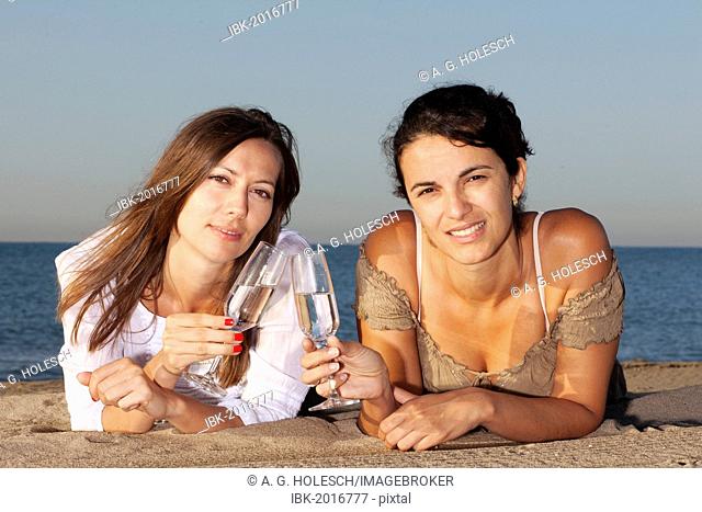 Two young women drinking champagne on a beach