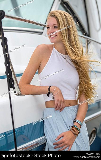 A teenage blonde model posing outdoors with boats