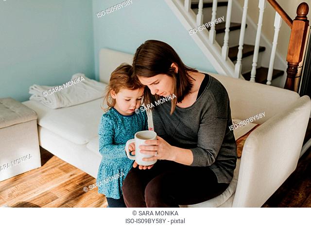 Female toddler and mother looking at coffee cup on sofa