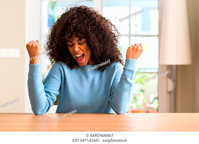 African american woman at home very happy and excited doing winner gesture with arms raised, smiling and screaming for success. Celebration concept