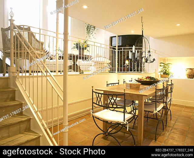 A modern, open plan split level yellow dining area, wooden table and metal chairs, tiled floor, steps up to sitting area