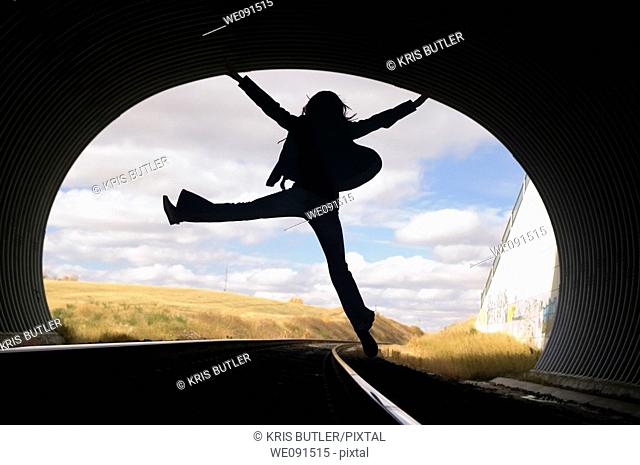 Silhouette of a young woman jumping in a train tunnel
