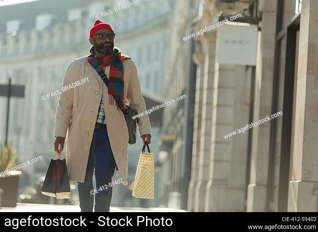 Man with shopping bags walking on sunny city sidewalk