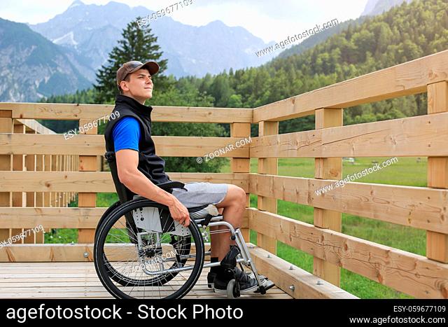 Disabled young man on a wheelchair on a wooden bridge path enjoying in nature looking at beautiful view