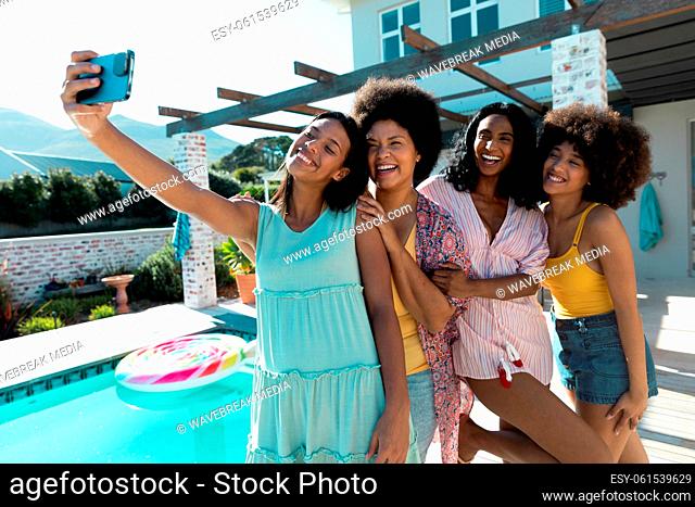 Carefree biracial female friends taking selfie over cellphone while having fun at poolside in summer