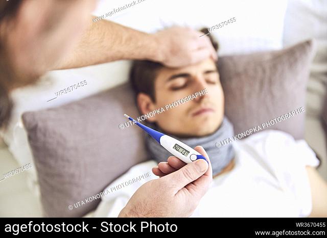 Close-up of doctor examining patient's temperature sleeping on bed at home