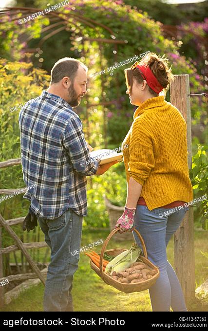 Couple with book and fresh harvested vegetables in summer garden