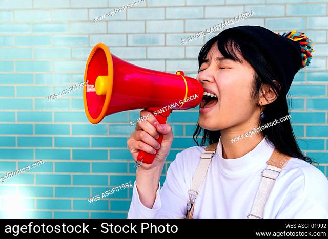 Woman shouting using megaphone in front of brick wall
