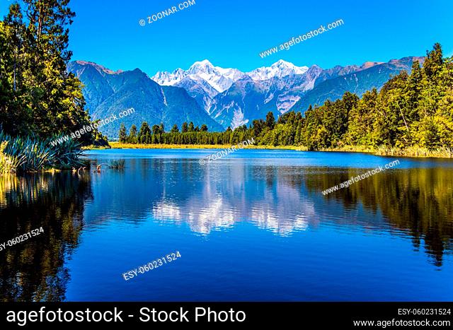 Magnificent snow-capped mountains surround the smooth, cold waters of Lake Matheson. The forests and Mount Cook and Mount Tasman