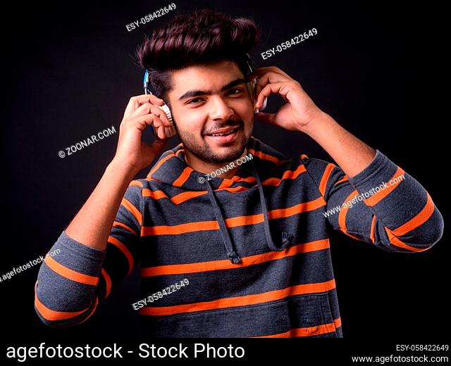 Studio shot of young handsome Indian man against black background