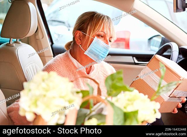 Frau mit Mundschutz in Auto Innenraum prüft Paket nach Abholung oder vor Übergabe