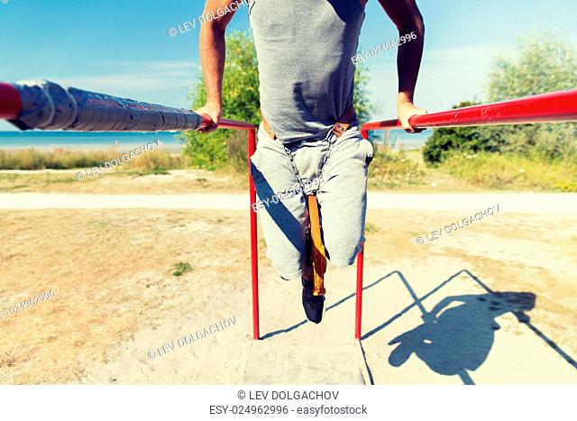 fitness, sport, exercising, training and lifestyle concept - close up of young man doing triceps dip with weight belt on parallel bars outdoors