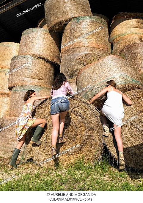 Girls climbing onto bale of hay