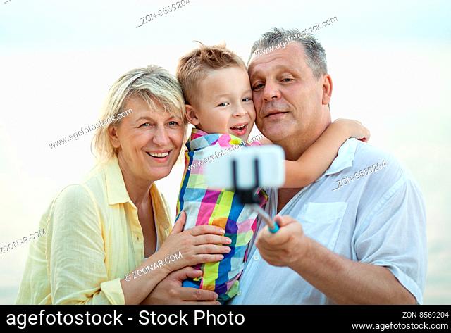 Happy grandparents holding little grandchild in arms outdoor and taking selfie stick picture together