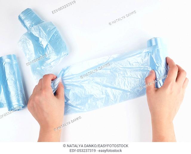 female hand unwinds a blue plastic bag for rubbish, white background