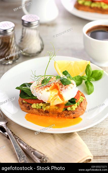 Breakfast. Best Eggs Benedict on a slice of toasted cereal bread with guacamole and spinach