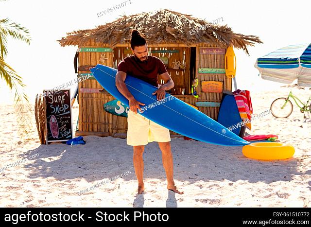 Mixed race man holding surf board on beach