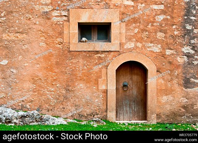 Abstract details of a brown stone wall with an old wooden closed vintage door and a small window