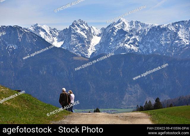 22 April 2023, Bavaria, Oberaudorf: Hikers walking in front of snow-capped mountains in the sunshine. Photo: Karl-Josef Hildenbrand/dpa