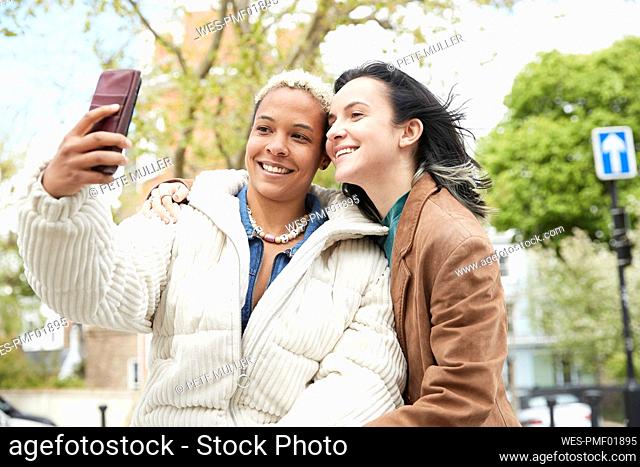 Happy woman taking selfie with girlfriend through mobile phone