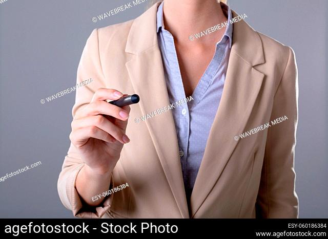 Midsection of caucasian businesswoman holding pen, isolated on grey background