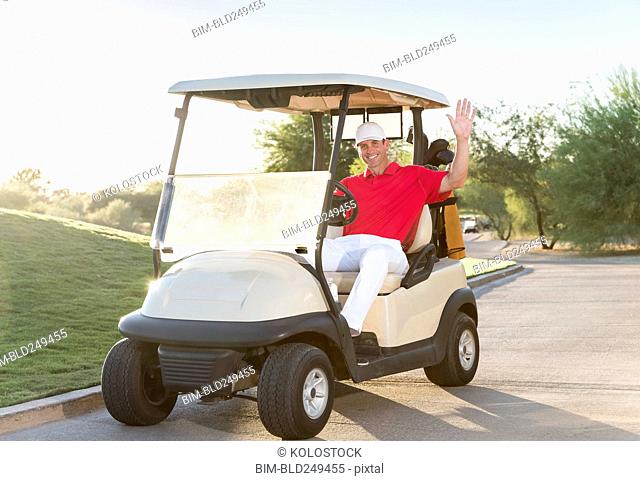 Portrait of Hispanic golfer waving in golf cart