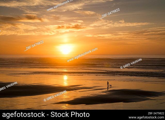 Woman walking dog at sunset on Tillicum Beach, central Oregon coast