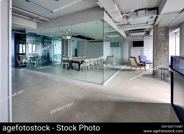 Meeting zone in the office in a loft style with white brick walls and concrete columns. Zone has a large wooden table with gray chairs and glass partitions