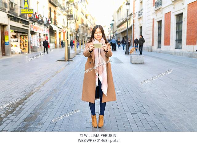 Spain, Madrid, young woman taking photos with a smartphone in the city