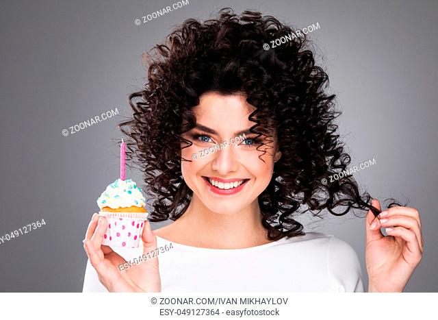Beautiful young woman holding small cake with colorful candle. Birthday, holiday. Studio portrait