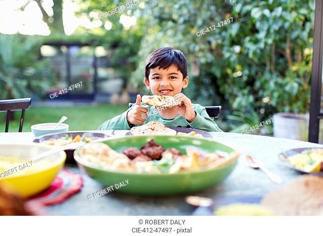 Portrait happy boy eating naan bread at patio table
