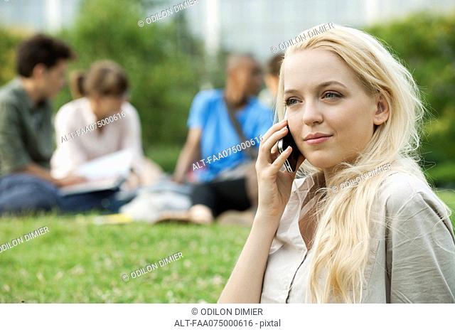 Young woman using cell phone, people in background, portrait