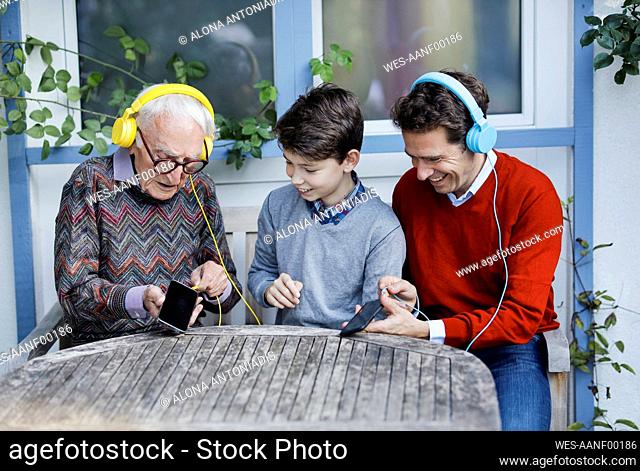 Niño con padre mirando al abuelo enchufando auriculares en un teléfono inteligente