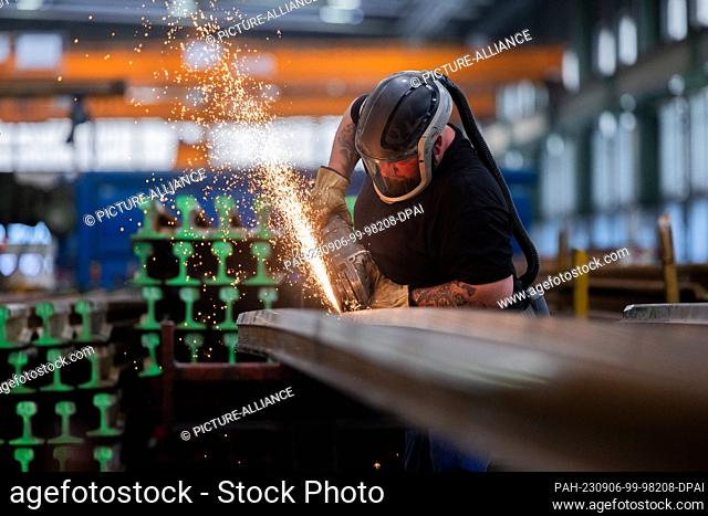 30 August 2023, North Rhine-Westphalia, Witten: A worker machines a switch tongue with an angle grinder at the plant for permanent way materials of Deutsche...