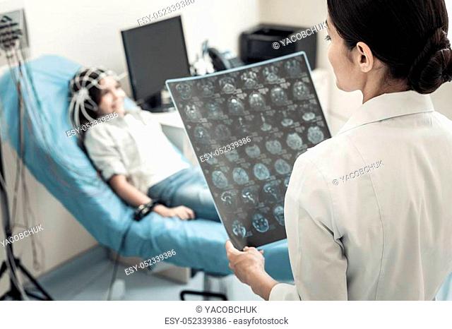 Modern radiography. Professional nice female neurologist holding an X ray scan and studying it while standing in her office