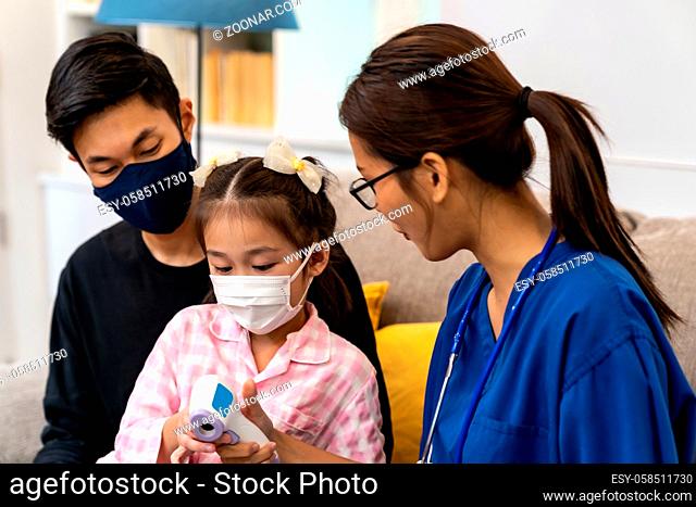 Asian female doctor show temperature using infrared thermometer to little girl child sit with her dad in living room while doctor visit at home