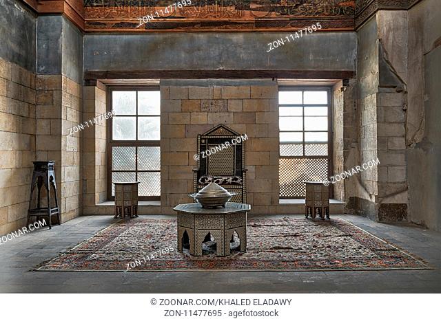 Cairo, Egypt - November 25, 2017: Hall at the palace of Prince Taz with stone bricks wall decorated by calligraphy with two windows, historic chair and tables