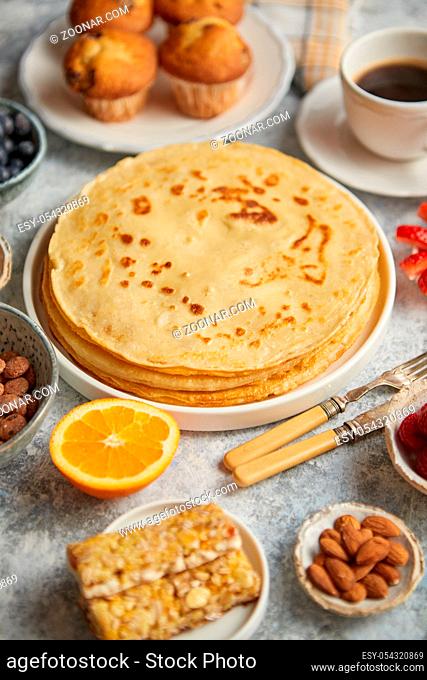 Various breakfast ingredients placed on stone table. With pancakes, muffins, fresh fruits, cupcakes, black coffee in cup. Flat lay. View from above