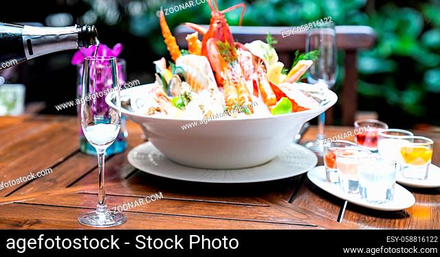 Waiter pouring white wine into wine glass and serving to customer in restaurant with big bowl seafood on ice in background