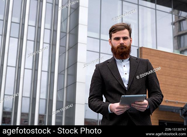 Modern Young bearded Business man standing with a digital tablet. Young hipster businessman holding tablet in hands outdoor