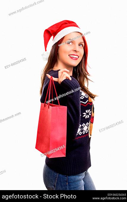 Holidays, shopping and presents. Beautiful young girl in winter clothes, wearing santa's hat, holding a shopping bag, isolated on white background
