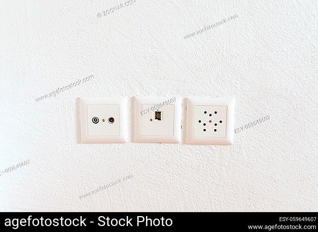 A close up view of sockets for television, internet, telephone and electricity on a white plaster wall