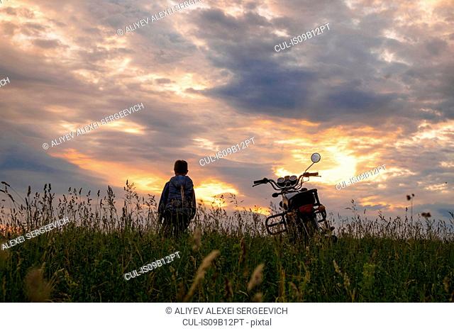 Boy in field with bicycle at sunset